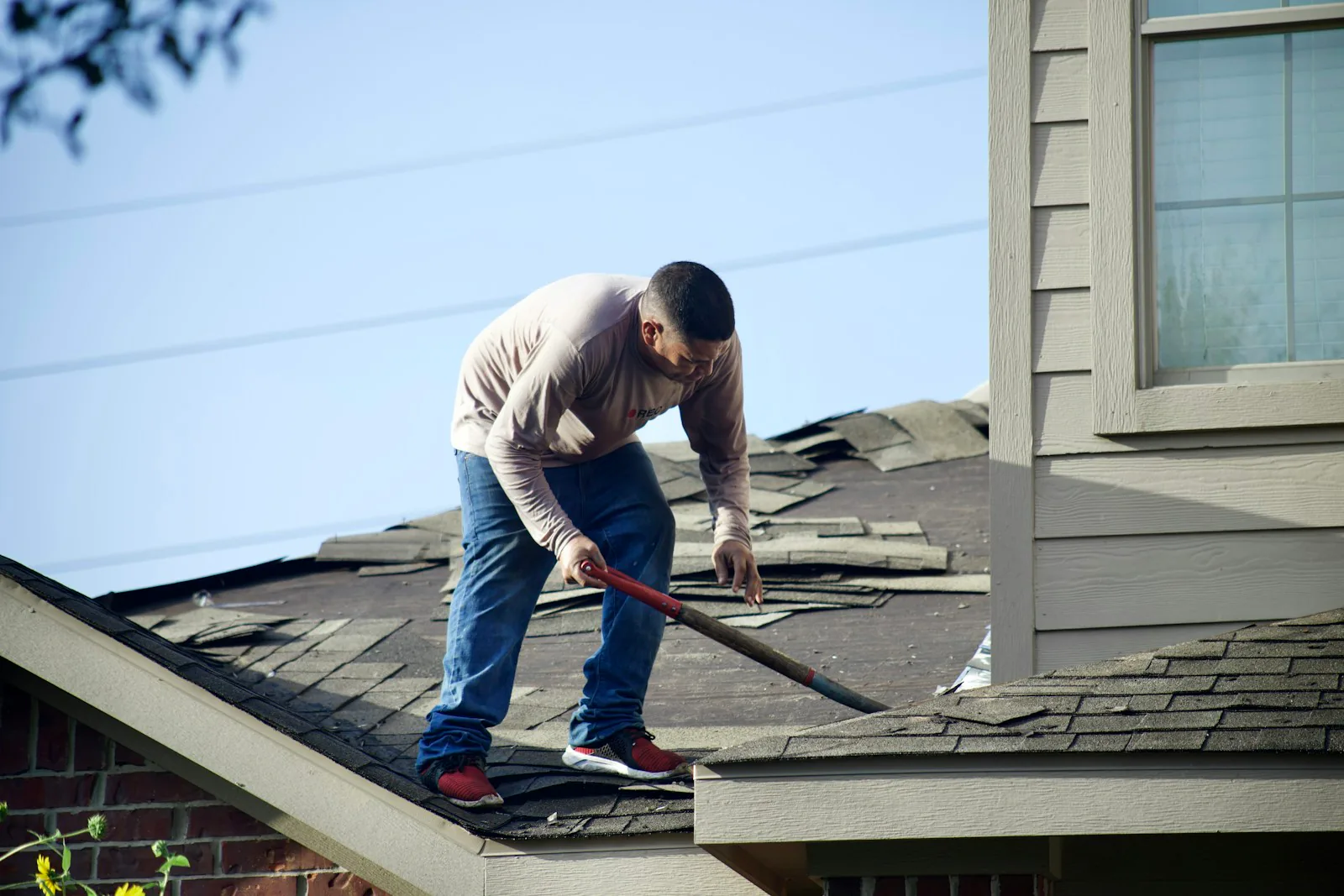 Damaged and lifted asphalt shingles being stripped from a residential roof in Commack, NY