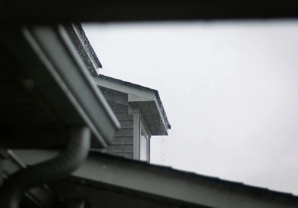 Rain running off the edge of a residential roof past the gutter line